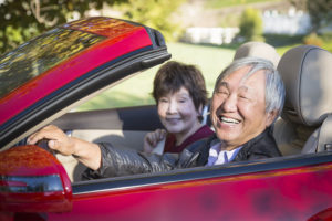 Smiling Asian senior couple in red convertible