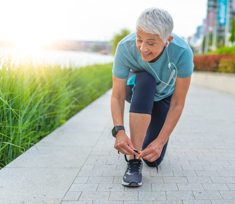 senior female runner kneels to tie shoe