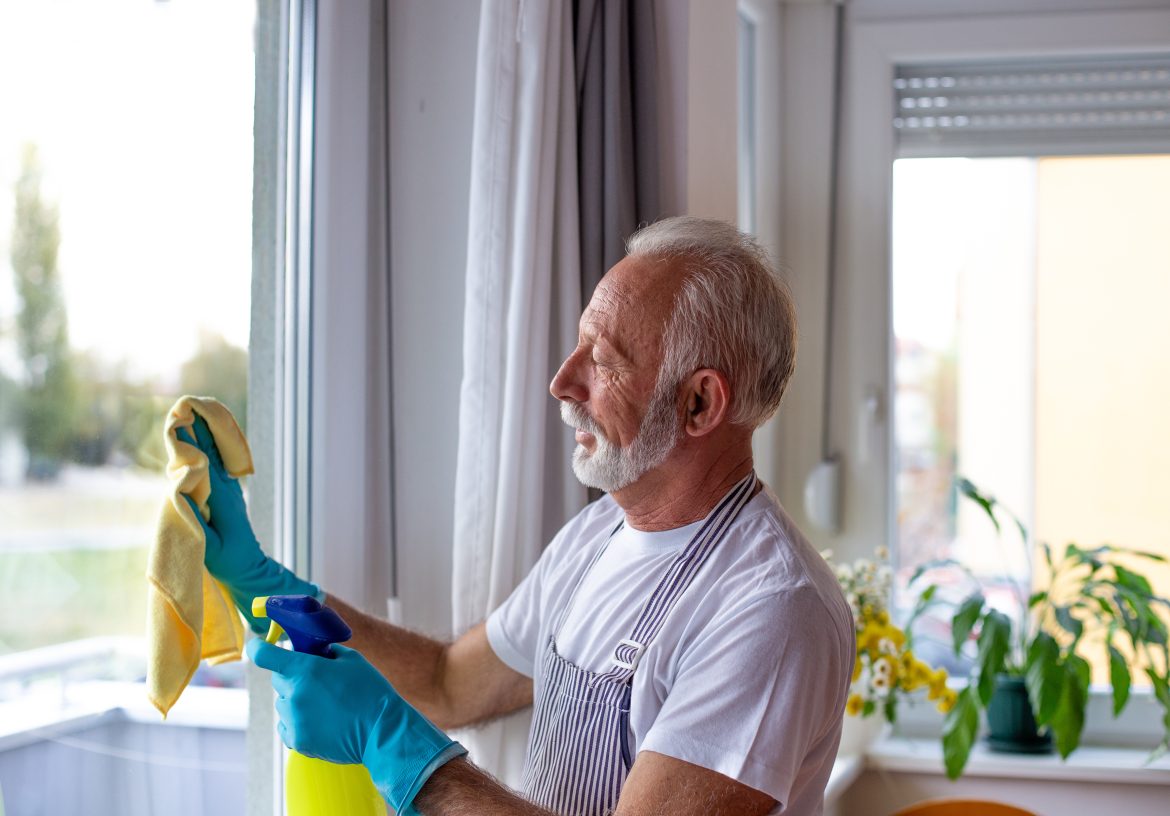 Senior man wearing rubber gloves and washing windows.