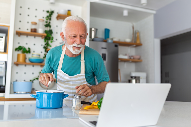 Senior man cooking while watching cooking video on laptop.