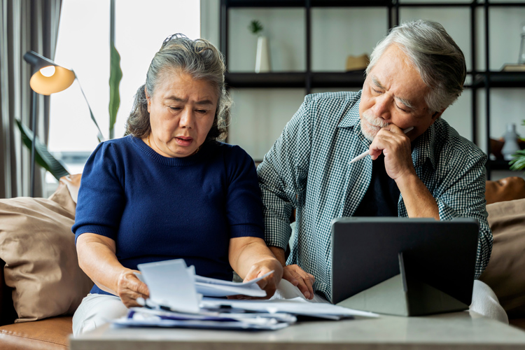 Older Asian couple reviewing stack of bills.