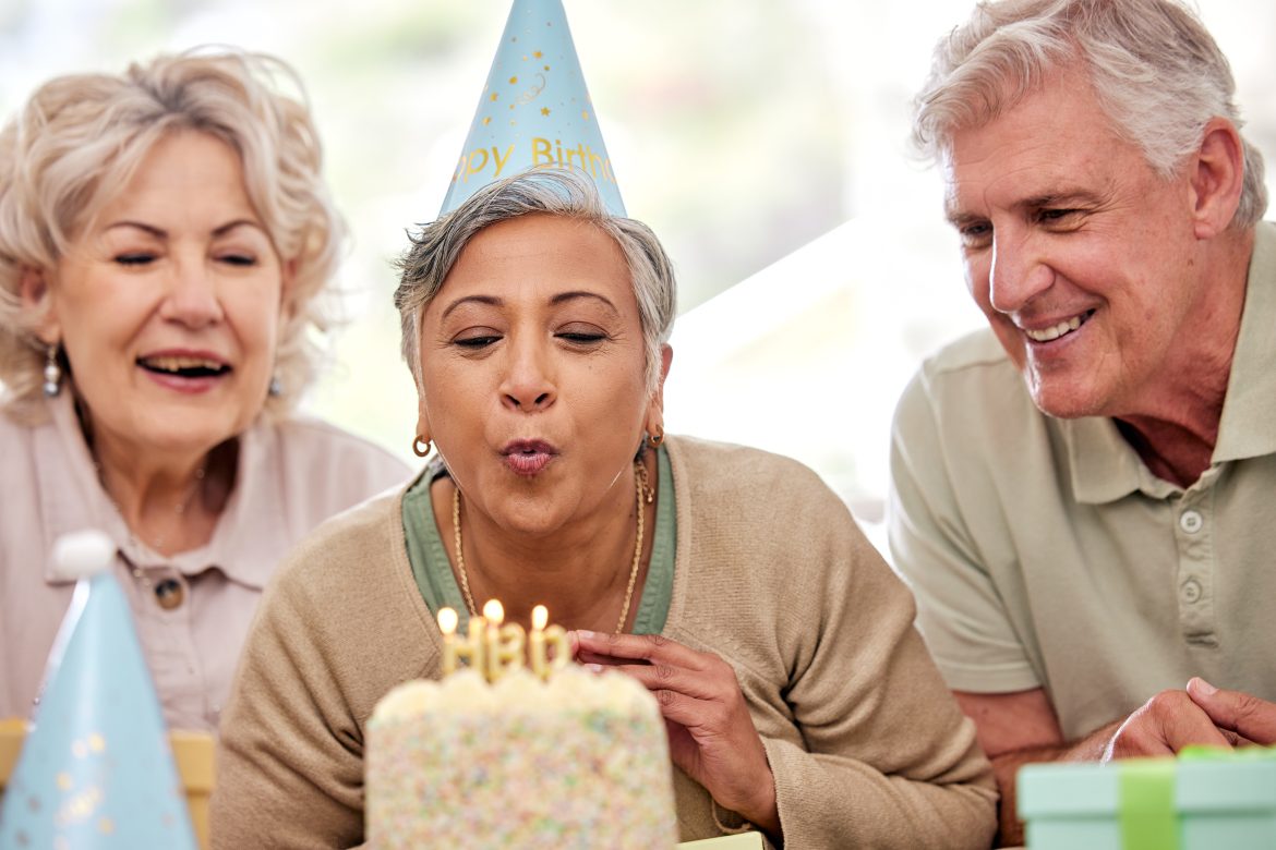 Woman in a senior living community blows out birthday candles as smiling friends look on.