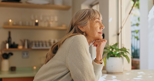Older woman looking out window and feeling confident and peaceful.