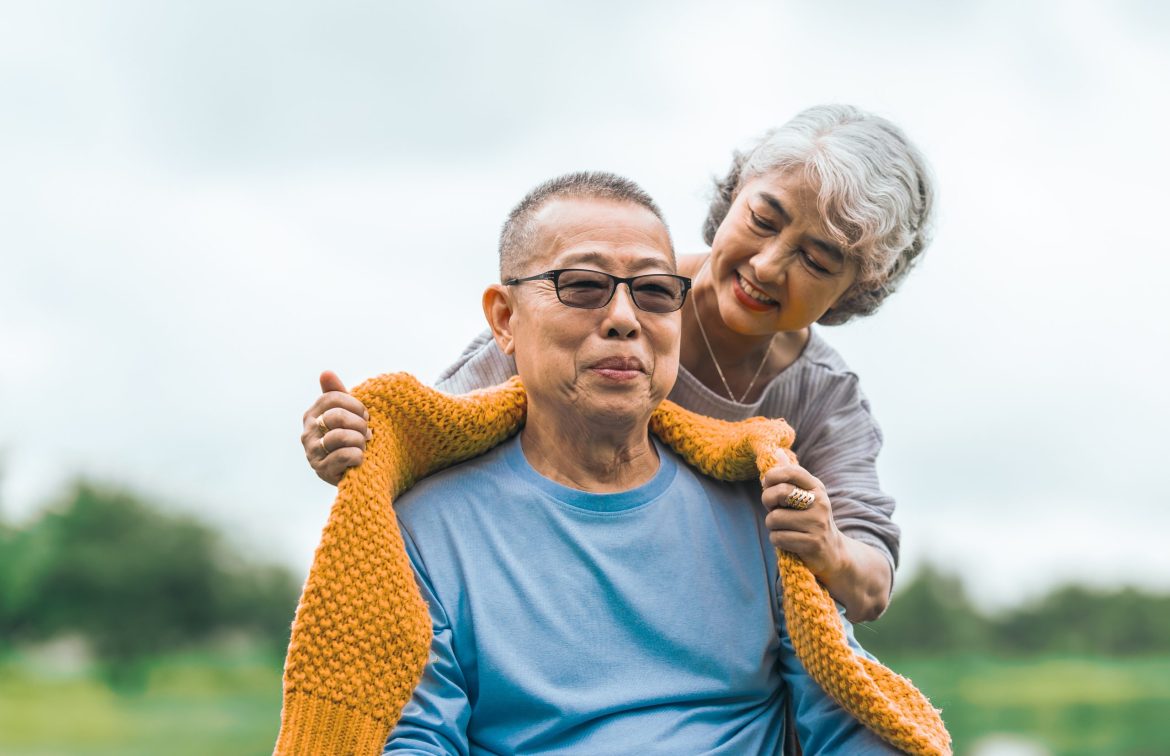 An Asian woman drapes a scarf around the neck of an Asian man in a wheelchair