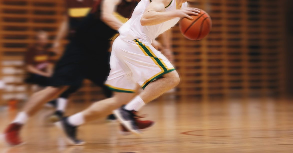 blurred photo of high school basketball players in action, showing only the torso down. 