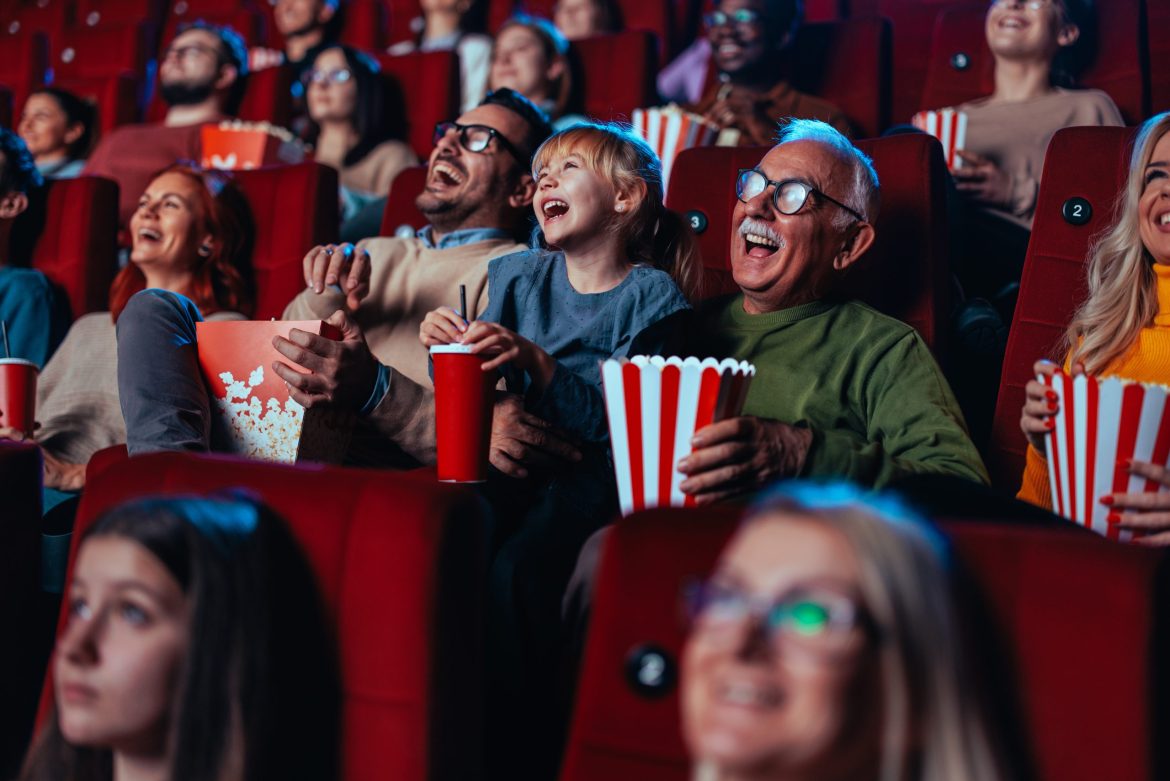 An audience in a movie theatre, featuring an older adult man up front.